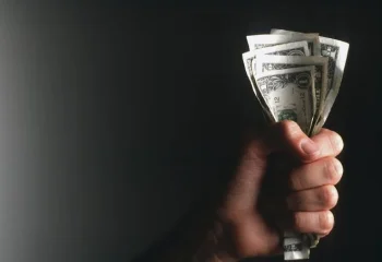 تصویر دست یک فرد در حالی که مقدار دلار در مشت دارد